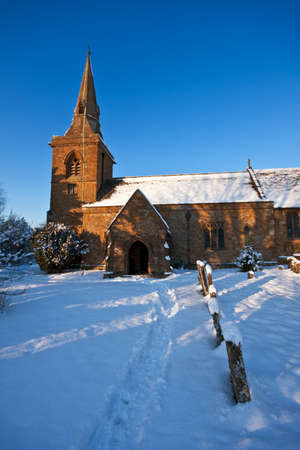 A traditional English village churchyard covered with snow on a sunny winter afternoon, with blue sky in the background.の写真素材