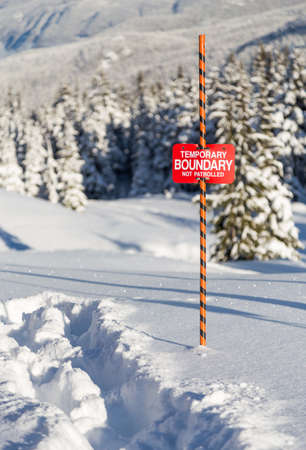 Tracks in the snow beside a ski area boundary sign.