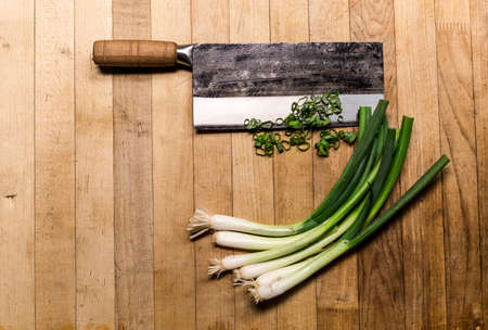 Chinese chopping knife with green onions on a wood cutting board.の写真素材
