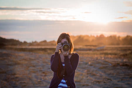 A girl taking a photo with a DSLR with the sunset in the background.の写真素材