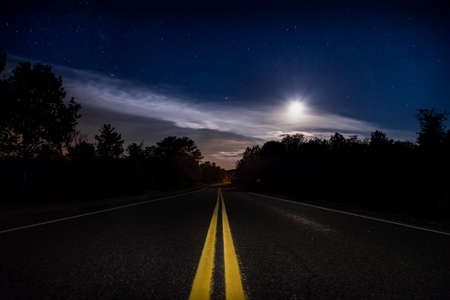 A empty road at night with the moon shining in the background.の写真素材
