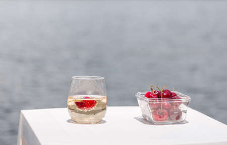 A bowl of cherries and a glass of champagne next to the lake.の写真素材