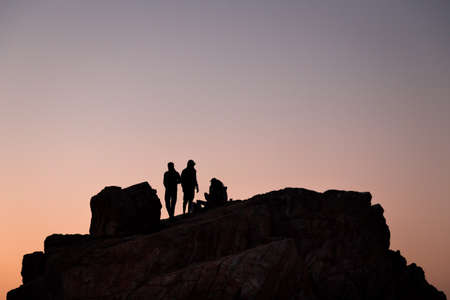 Silhouette of teens handing out atop a rock at sunset.の写真素材