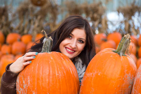 A young brunette woman holding a pumpkin in front of a row of pumpkins on a farm.の写真素材