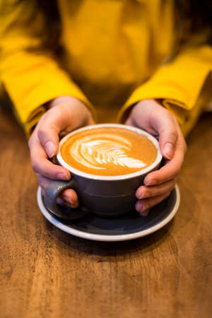 Female hands holding a latte on a wooden table.の写真素材