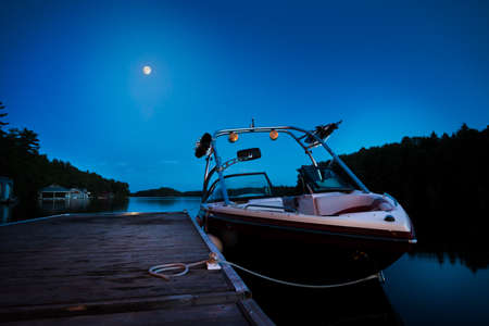A wakeboard boat docked on Lake Joseph in the evening with the moon in the background.の写真素材