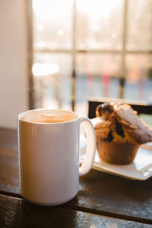 A blueberry muffin and a cup of coffee latte on a wood table with rays sunlight.の写真素材