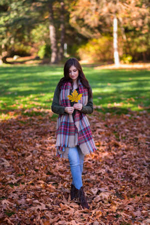 A young brunette woman in a park surrounded by fall leaves.
