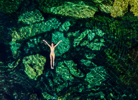 Overhead shot of a attractive young brunette woman in a bikini floating in the Cristalino cenote near Tulum, Mexico.の写真素材