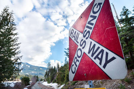 A red railway crossing sign with railroad tracks and a mountain in the background.の写真素材