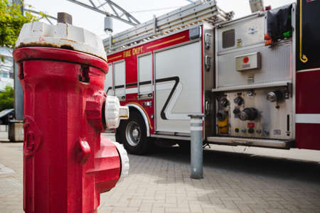 A red fire hydrant in front of a large red fire truck with plumbing for water hose attachments...