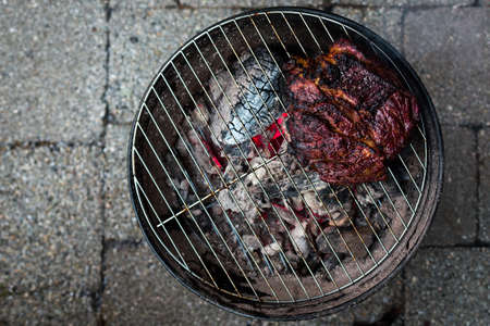 A top down view of a large beef brisket and being barbequed on a small charcoal hibachi grill with glowing coals underneath.の写真素材