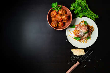 An overhead shot of a plate of rustic spaghetti and meatballs with a bowl of meatballs, parmesean cheese, and fresh parsley.の写真素材