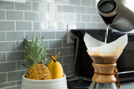 Close-up of a a electric kettle pouring hot water into a drip coffee flask with a fruit bowl in the background.の写真素材