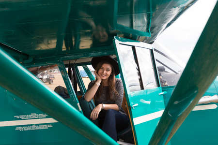 Cute young brunette hipster girl sitting in a vintage small aircraft smiling.