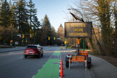 NORTH VANCOUVER, BC, CANADA - MAR 21, 2020: A electronic roadside sign displaying information related to the Coronavirus outbreak with a single car passsing by.のeditorial素材