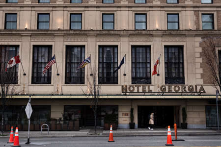 DOWNTOWN VANCOUVER, BC, CANADA - MAR 23, 2020: A single person walking in front of the Hotel Georgia with a medical facemask on during the COVID-19 pandemic.のeditorial素材