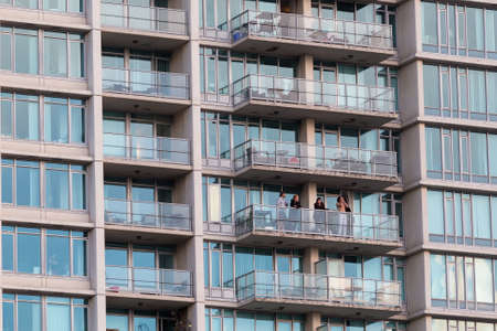 DOWNTOWN VANCOUVER, BC, CANADA - MAR 24, 2020: A couple that is self quarantining coming out on their balcony at 7pm to cheer for Canadian health care workers.のeditorial素材