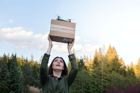 Attractive smiling young brunette woman holding a package that has been delivered by an autonomous...