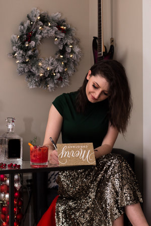 Attractive young brunette woman writing a Christmas card with a cocktail.