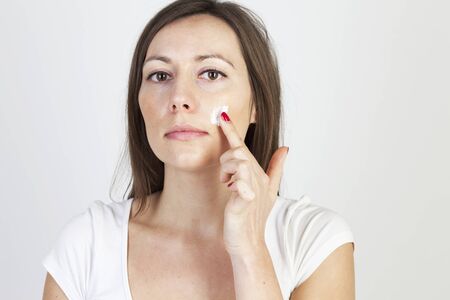 attractive caucasian woman putting lotion on her faceの写真素材
