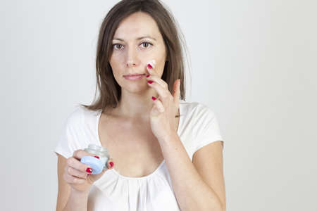 attractive caucasian woman putting lotion on her faceの写真素材