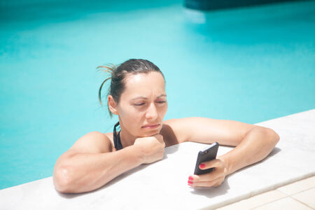 Woman reading the smart phone in poolの写真素材