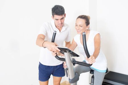 Personal trainer helps woman with spinning exercise