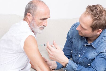 Setting an injection on the arm of an elderly man with grey beardの写真素材