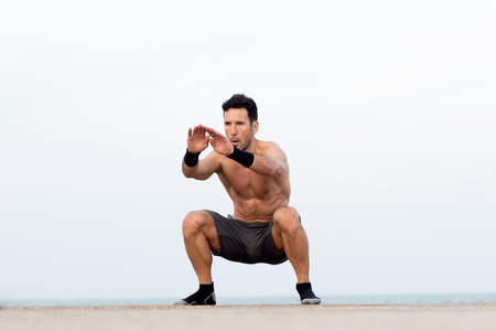 Athletic man makes squats by the seaの写真素材