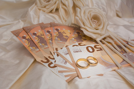 Wedding rings and banknotes with a wedding dress on the backgroundの写真素材
