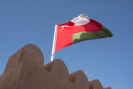 Scalloped walls of the Nahkal Fort and its flag in the wind (Oman)のeditorial素材