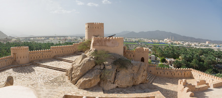 Walls and turrets of the Fort of Nahkal and the village with the mosque in the background (Oman)のeditorial素材