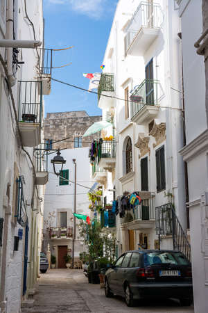 Monopoli, Italy - 20 August 2021: Characteristic alley with clothes hanging out to dry and parked car in the center of Monopoli (Puglia)のeditorial素材