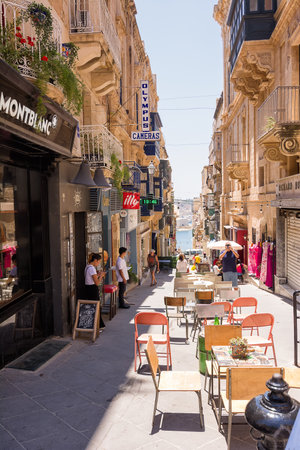 Valletta, Malta - 17 June 2023: Street with building and cafe tables at restaurants in Valletta,...