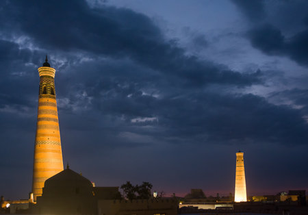Night view of the Juma and Islam Khodja minarets illuminated in the old city of Khiva, Uzbekistan, highlighting the city's iconic Islamic architecture.の写真素材