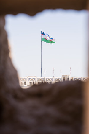 Uzbek flag waving in the wind, seen through a hole in the ancient city wall of Khiva, Uzbekistanの写真素材