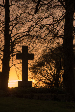 Ancient cross tombstone silhouetted at sunsetの写真素材