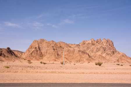 Red rocky desert with a mountain in the background and power lines in the foregroundの写真素材