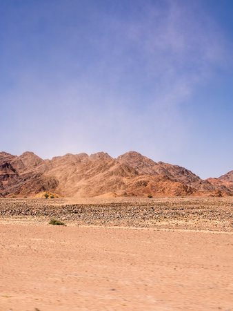 Red rocky desert detail with distant mountains and a wind blown cloud of dustの写真素材