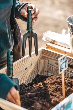 Gardening, a fantastic hobby. Close up of farmer's hands working in wooden box with soil and garden tools, while preparing for planting vegetables or flowers. Vertical shot. Selective focusの写真素材