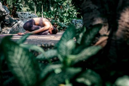 Full-length shot of caucasian woman sitting in Child's pose, Balasana while practicing yoga outdoors, in a garden. Healthy lifestyle and relaxation conceptの写真素材