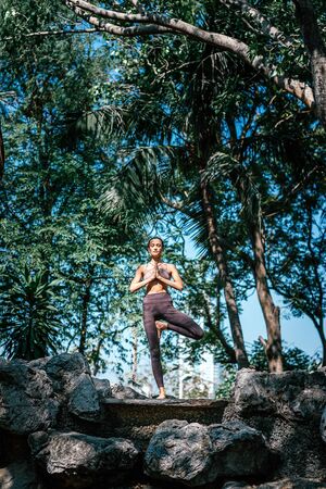 Full-length shot of caucasian woman standing in Tree pose, Vrksasana while practicing yoga outdoors, in a garden. Healthy lifestyle and relaxation conceptの写真素材
