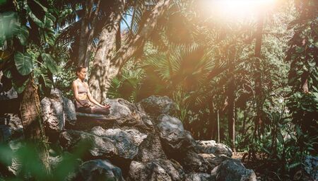 Full-length shot of caucasian woman sitting in Easy Seated pose, Sukhasana while practicing yoga outdoors, in a garden. Healthy lifestyle and relaxation conceptの写真素材