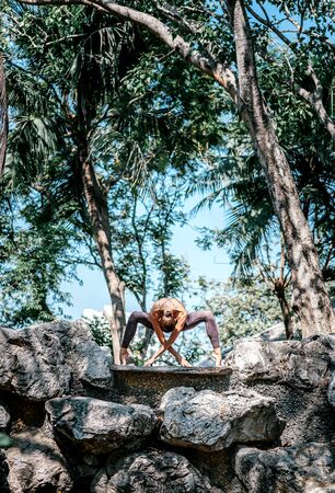 An Inspiration for Better Living. Full-length shot of caucasian woman standing in Spider pose, while practicing yoga outdoors, in the nature park. Healthy lifestyle and relaxation conceptの写真素材