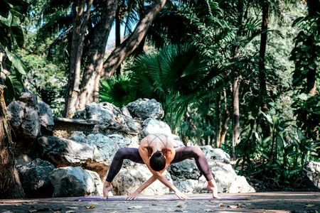 Be In the Moment. Full-length shot of caucasian woman standing in Spider pose, while practicing yoga outdoors, in a garden. Healthy lifestyle and relaxation conceptの写真素材