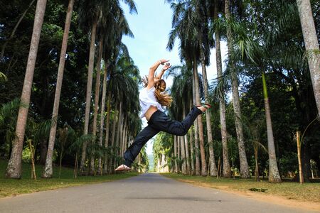 Girl jumping in the middle of a palm trees avenue