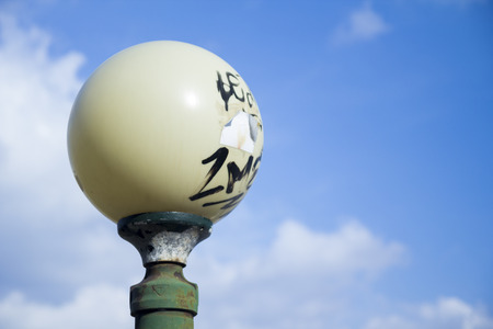 A round lamppost with graffiti on it, shot against the cloudy skyの写真素材