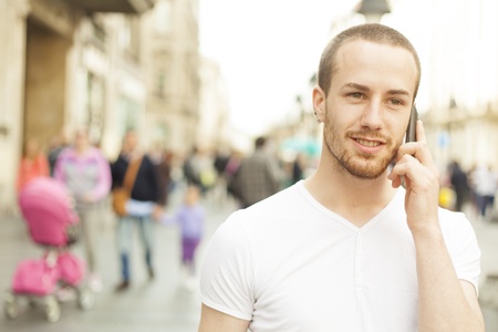 Young Man with mobile phone walking, background is blured cityの写真素材