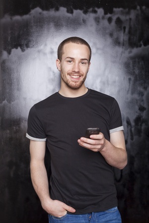 Smiling guy with smartphone typing SMS, studio shot on black backgroundの写真素材